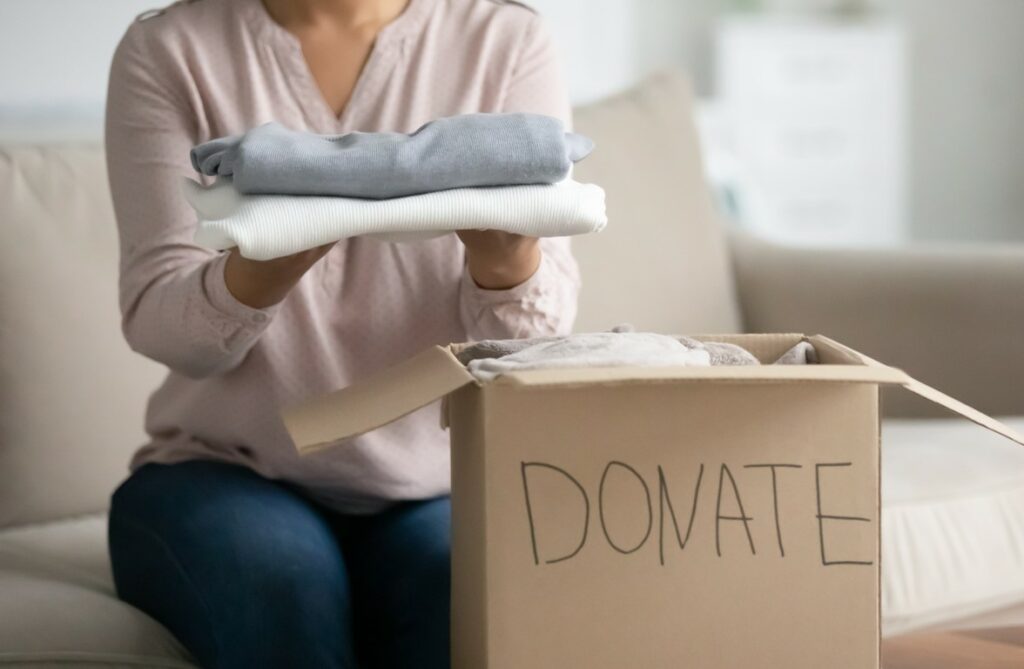 Homeowner places folded clothing into cardboard box labeled “Donate”