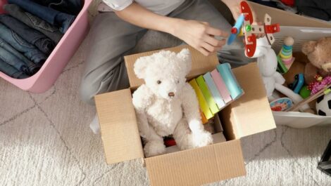 Person sorts toys and clothing into boxes while sitting on carpet