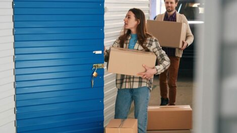 A woman and a man carry cardboard boxes into their self storage unit.