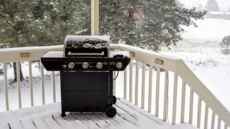 A black barbecue grill sits on a snow-covered back porch.